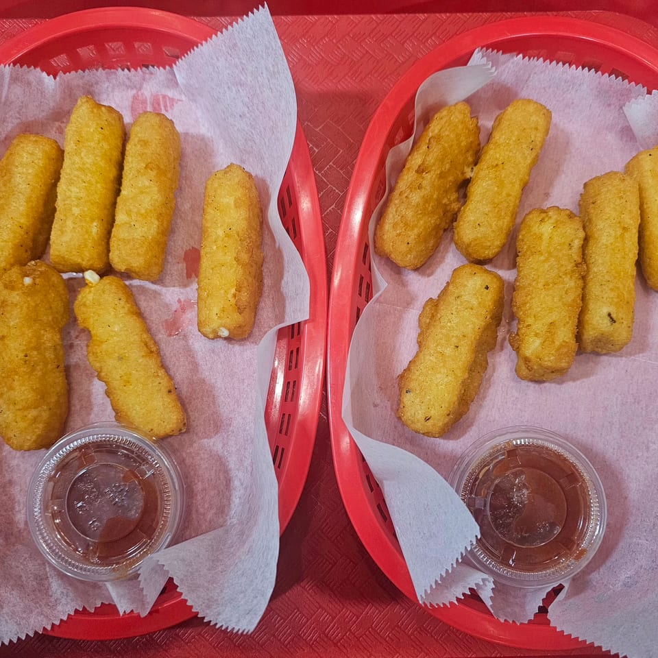 Two red baskets hold golden fried snack sticks on paper liners, each accompanied by a small cup of dipping sauce.